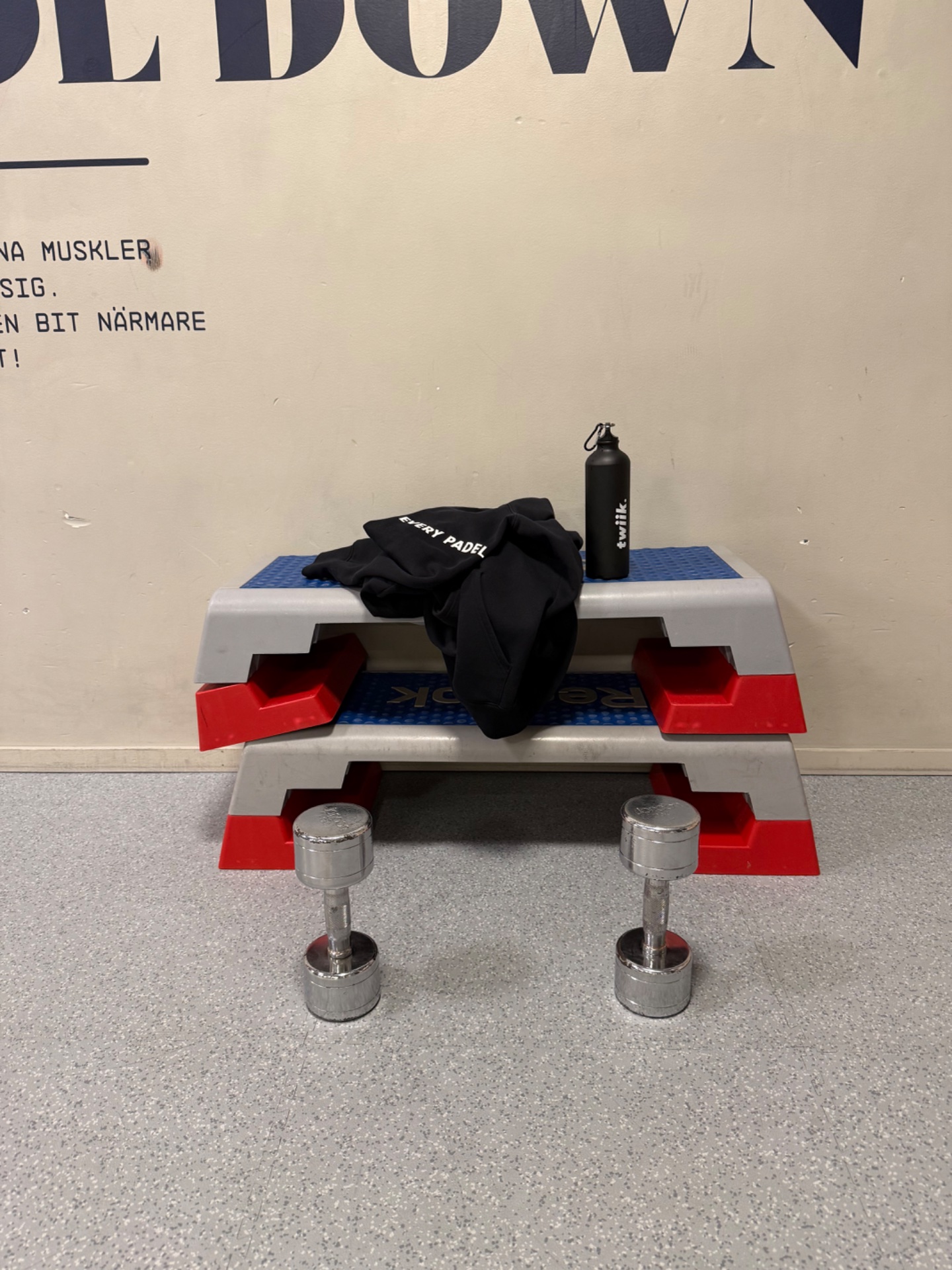 A gym setup featuring dumbbells, a padel paddle, and workout gear laid out on gym benches—ready for a strength training session!