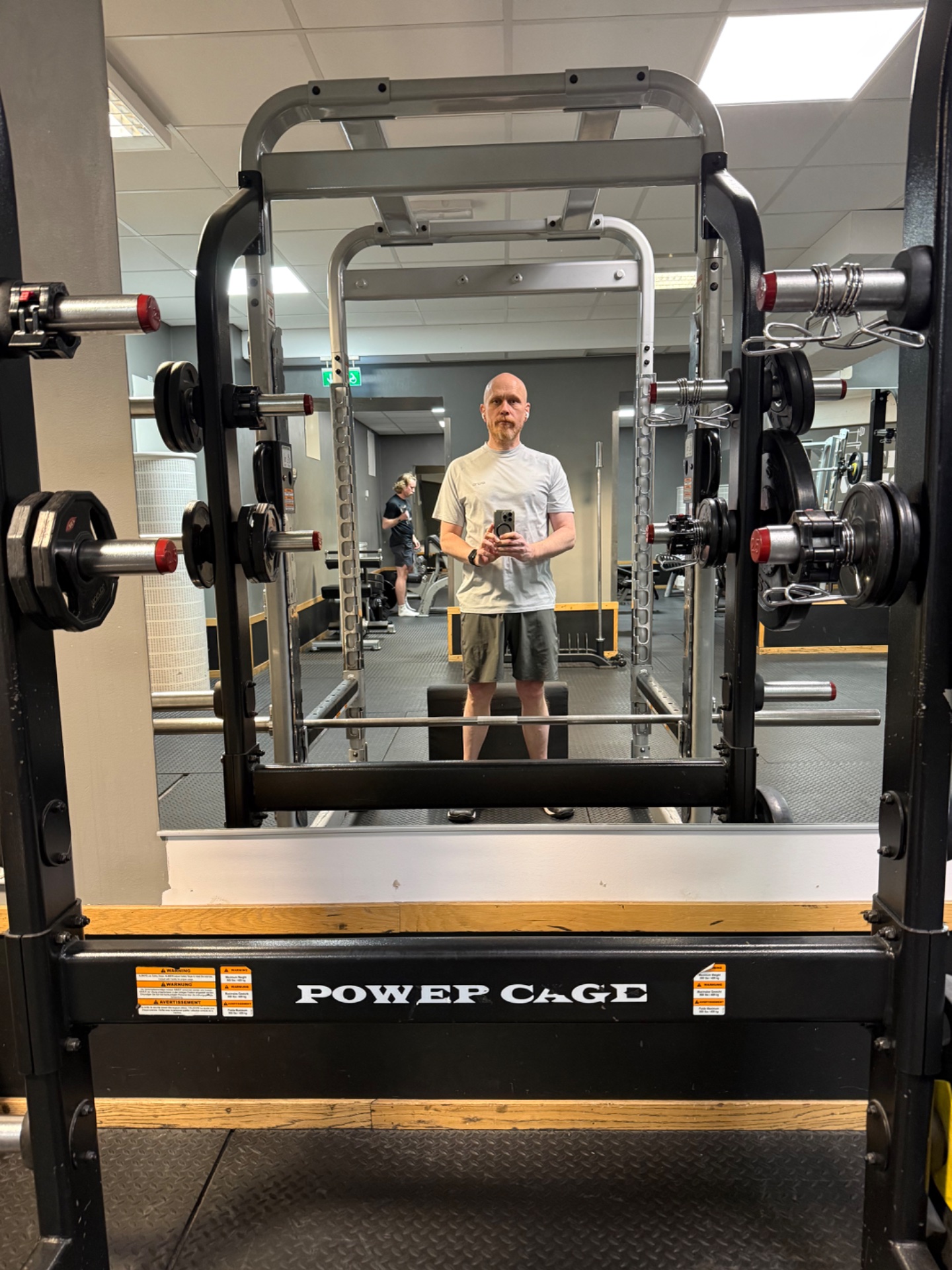 Gym selfie at a Power Cage with loaded barbells on both sides, clearly set up for weightlifting and resistance training. This is classic strength training equipment for squats, bench press, and other barbell exercises.