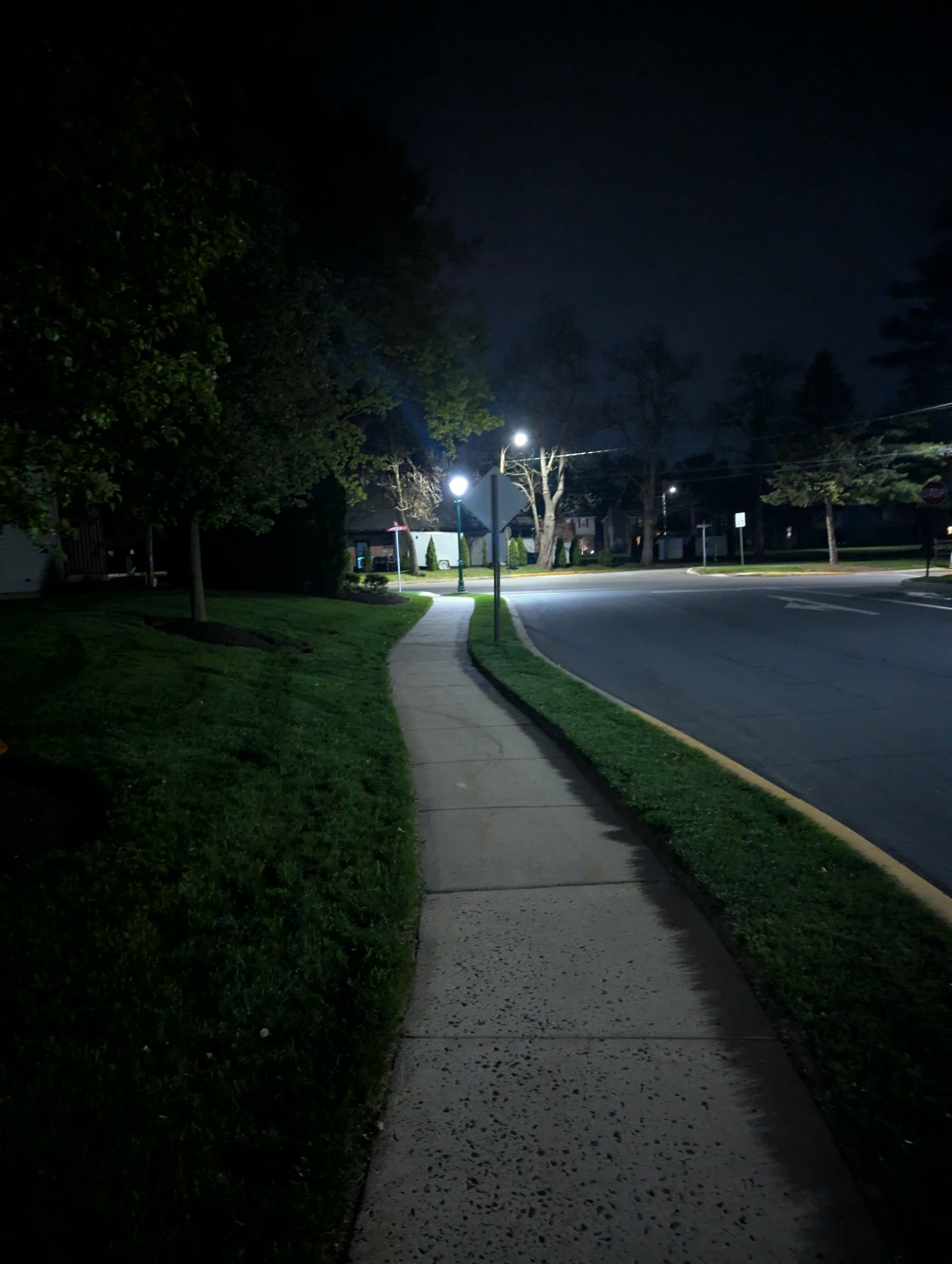 A nighttime walk or run through a well-lit suburban neighborhood path. The scenic sidewalk route with street lighting suggests an evening cardio session outdoors.