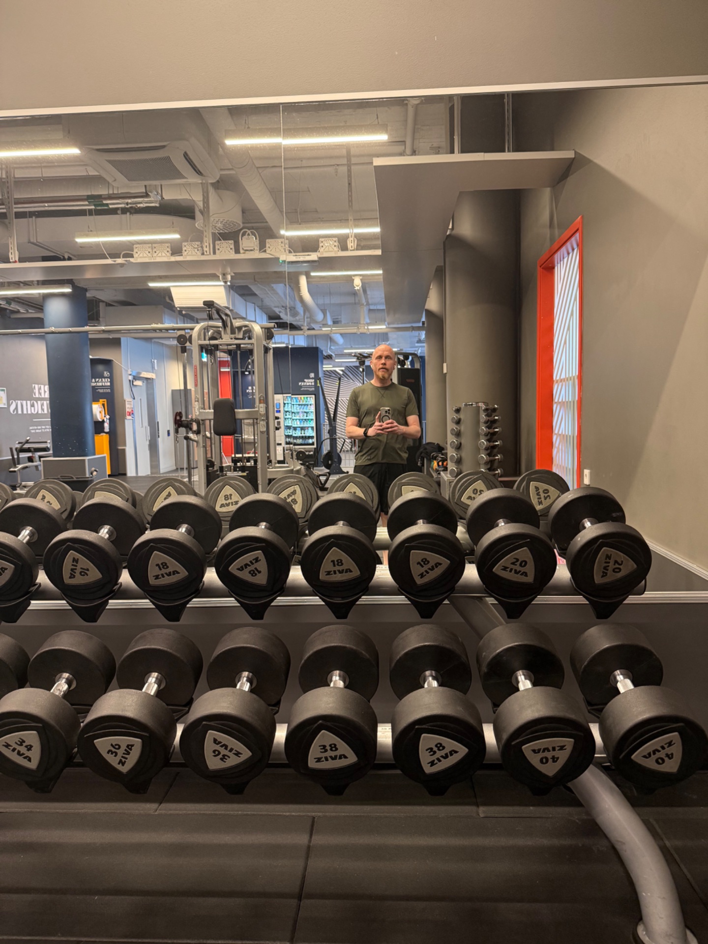 Gym selfie at the dumbbell rack! This person is capturing their strength training session surrounded by a full set of weights, ready for some serious resistance work.