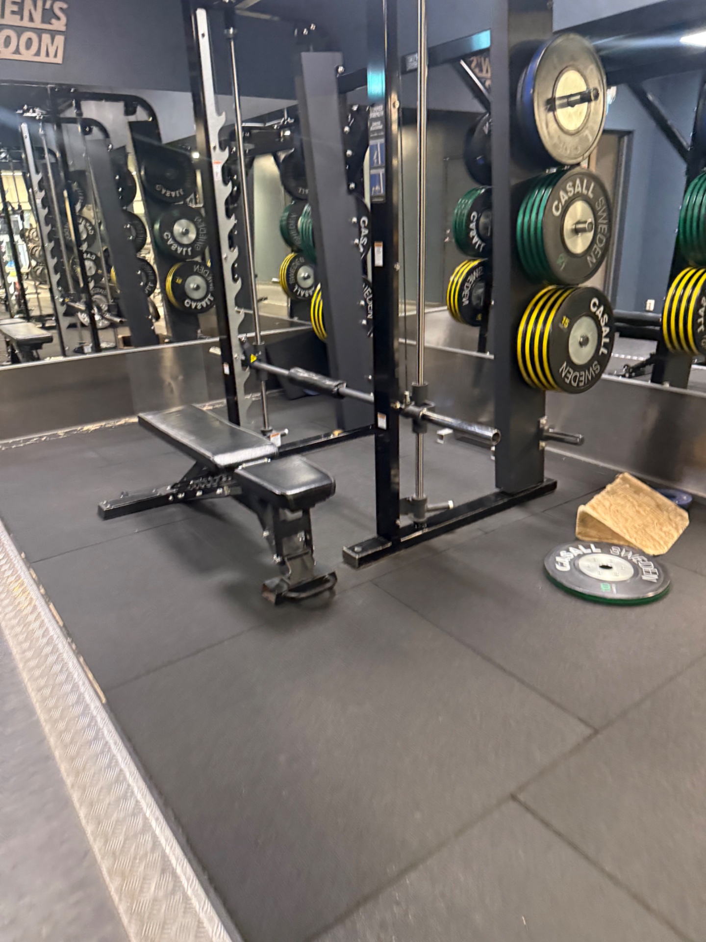 A well-equipped strength training gym setup featuring multiple squat racks, barbells with colored weight plates (green and yellow), and a padded lifting floor—perfect for powerlifting, CrossFit, and resistance training workouts!