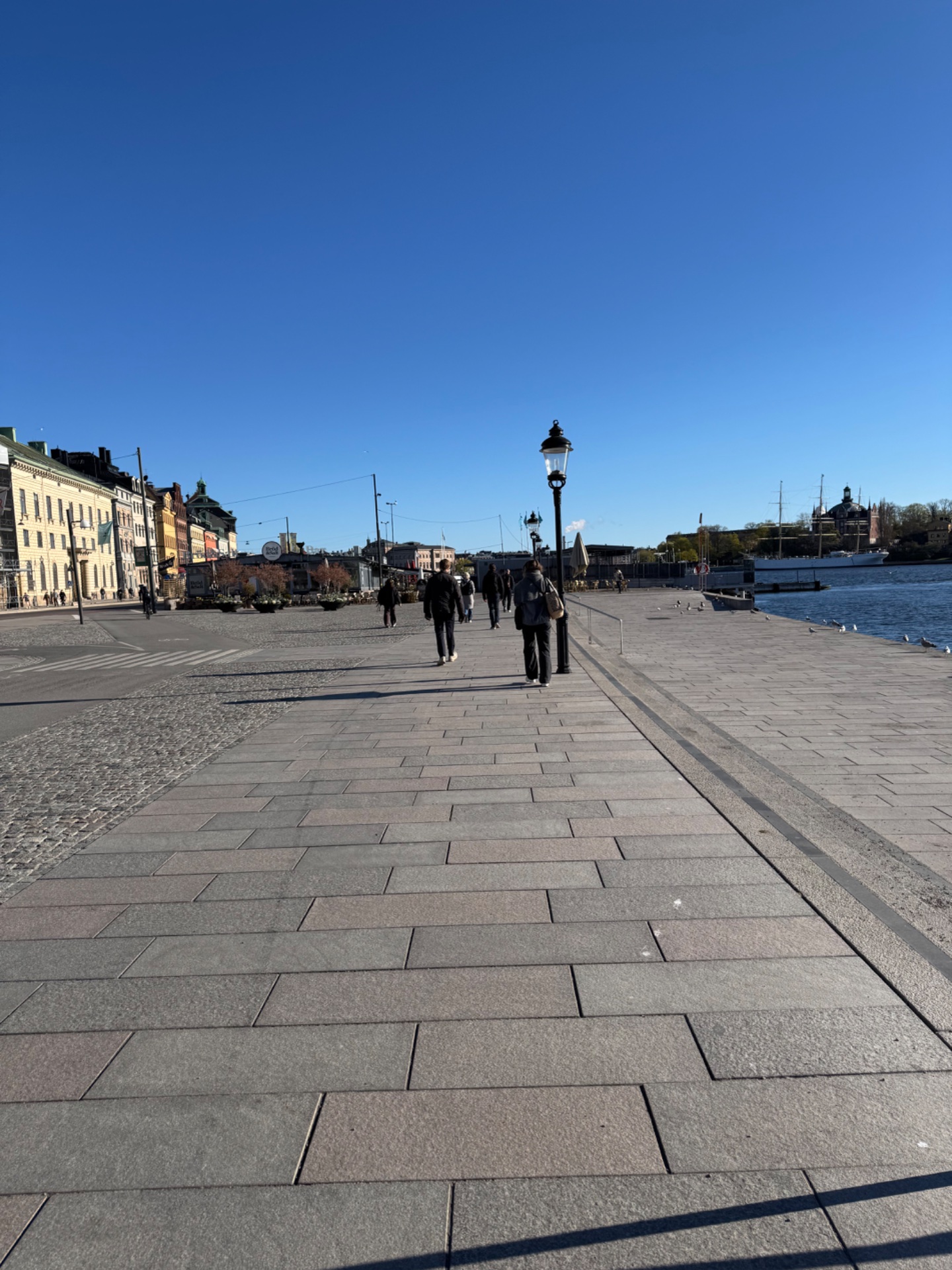 A scenic waterfront walk through what appears to be a Nordic harbor district on a beautiful clear day. Perfect casual cardio activity combining fresh air and sightseeing!