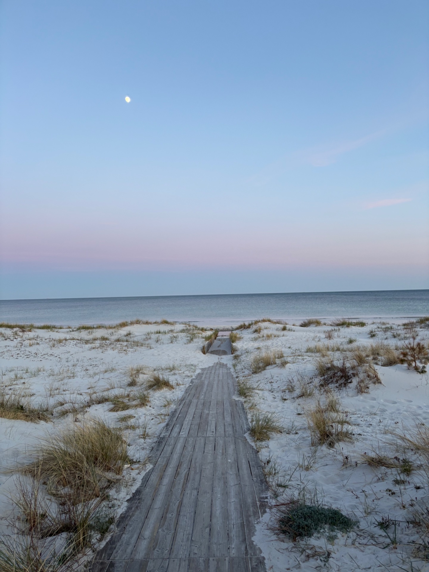 A scenic beach walk or run along a serene coastline at dusk, with a peaceful wooden boardwalk leading through the sandy dunes toward the water's edge.