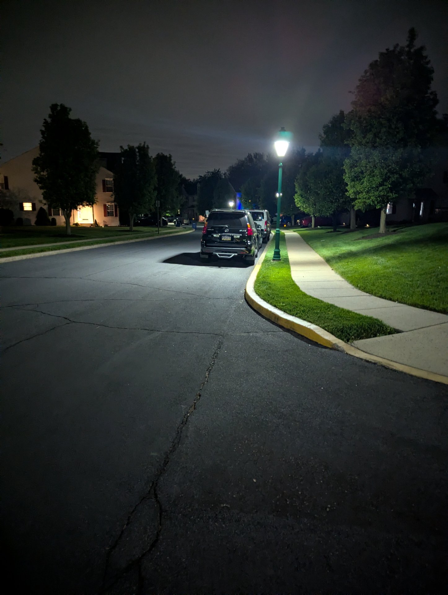 An evening neighborhood walk or run captured under street lights, showing a scenic tree-lined residential street perfect for outdoor cardio activity.