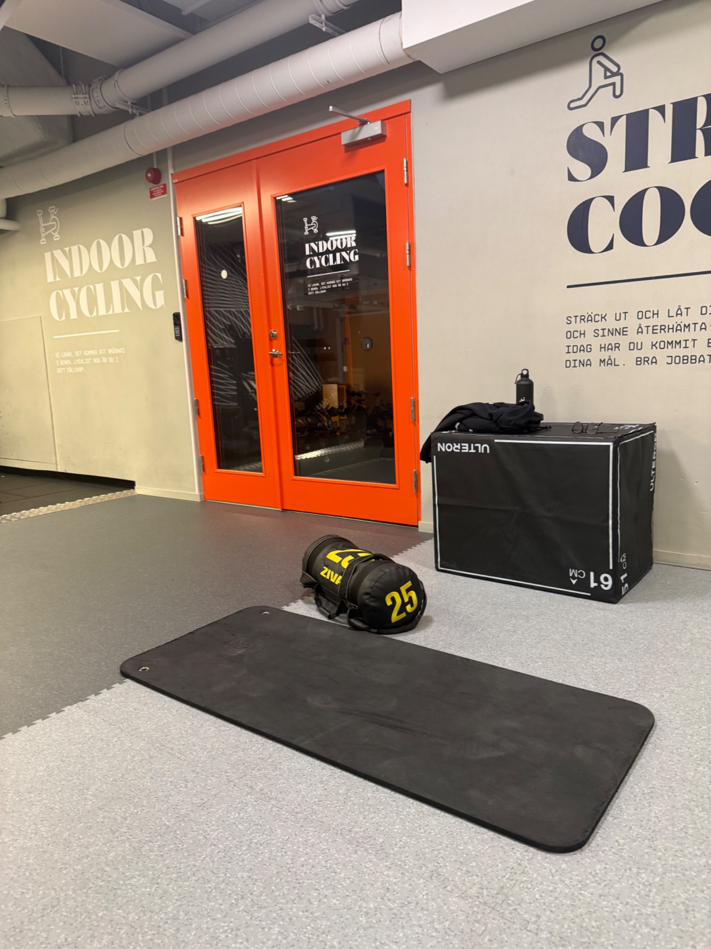 A strength training setup at an indoor cycling studio featuring a medicine ball (25 lbs), exercise mat, and plyometric box for functional fitness and cross-training exercises.