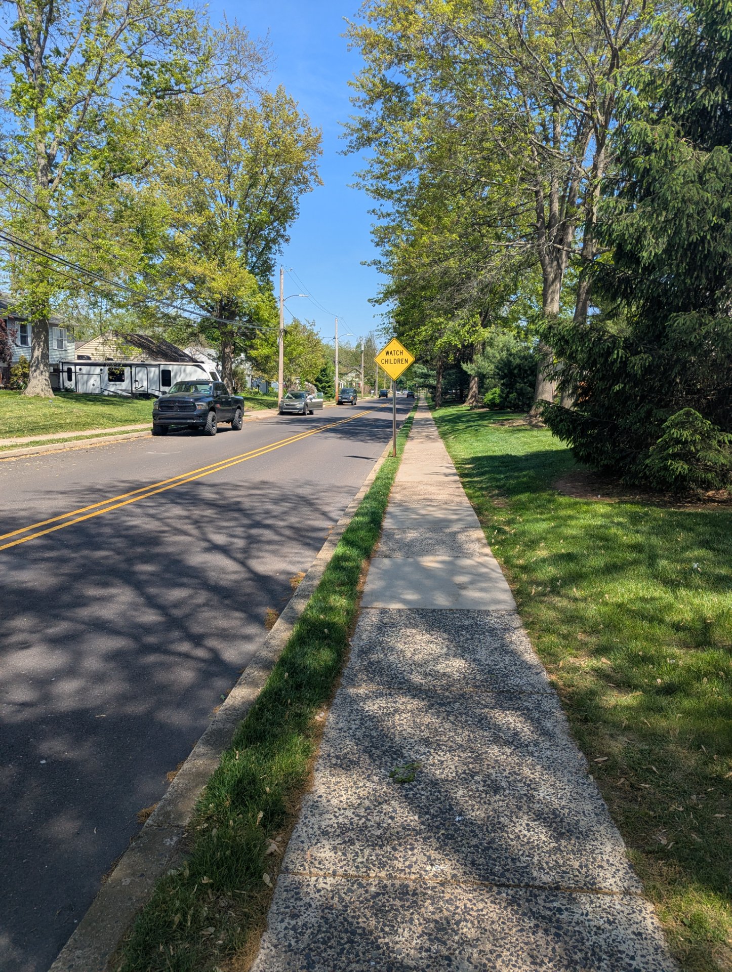 A scenic neighborhood walk or run along a tree-lined residential street with a clear sidewalk and beautiful weather—perfect conditions for outdoor cardio activity!