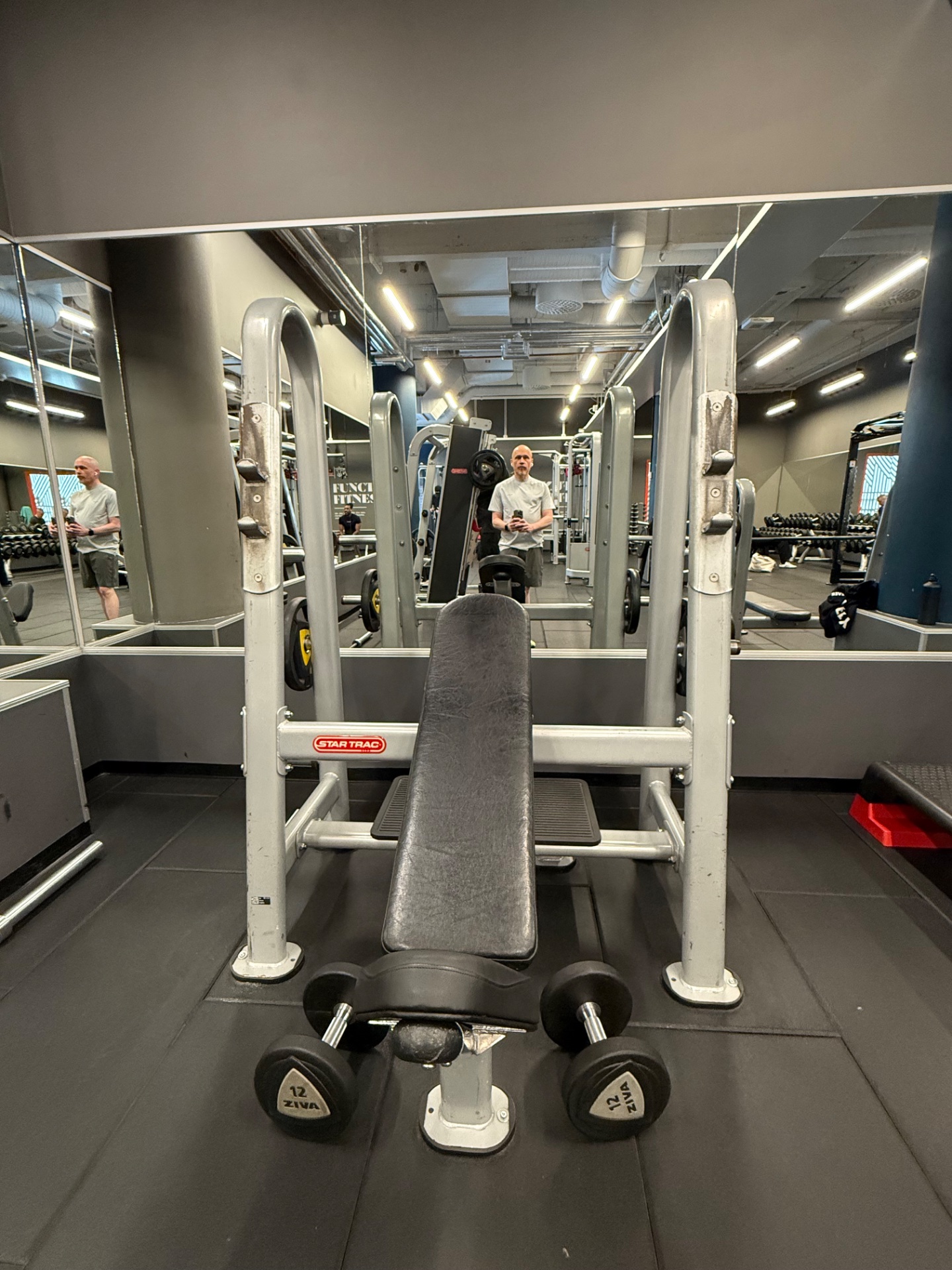 A gym workout session featuring resistance training on a Star Trac machine with dumbbells ready for use. This is a solid strength-focused session at a well-equipped fitness facility.