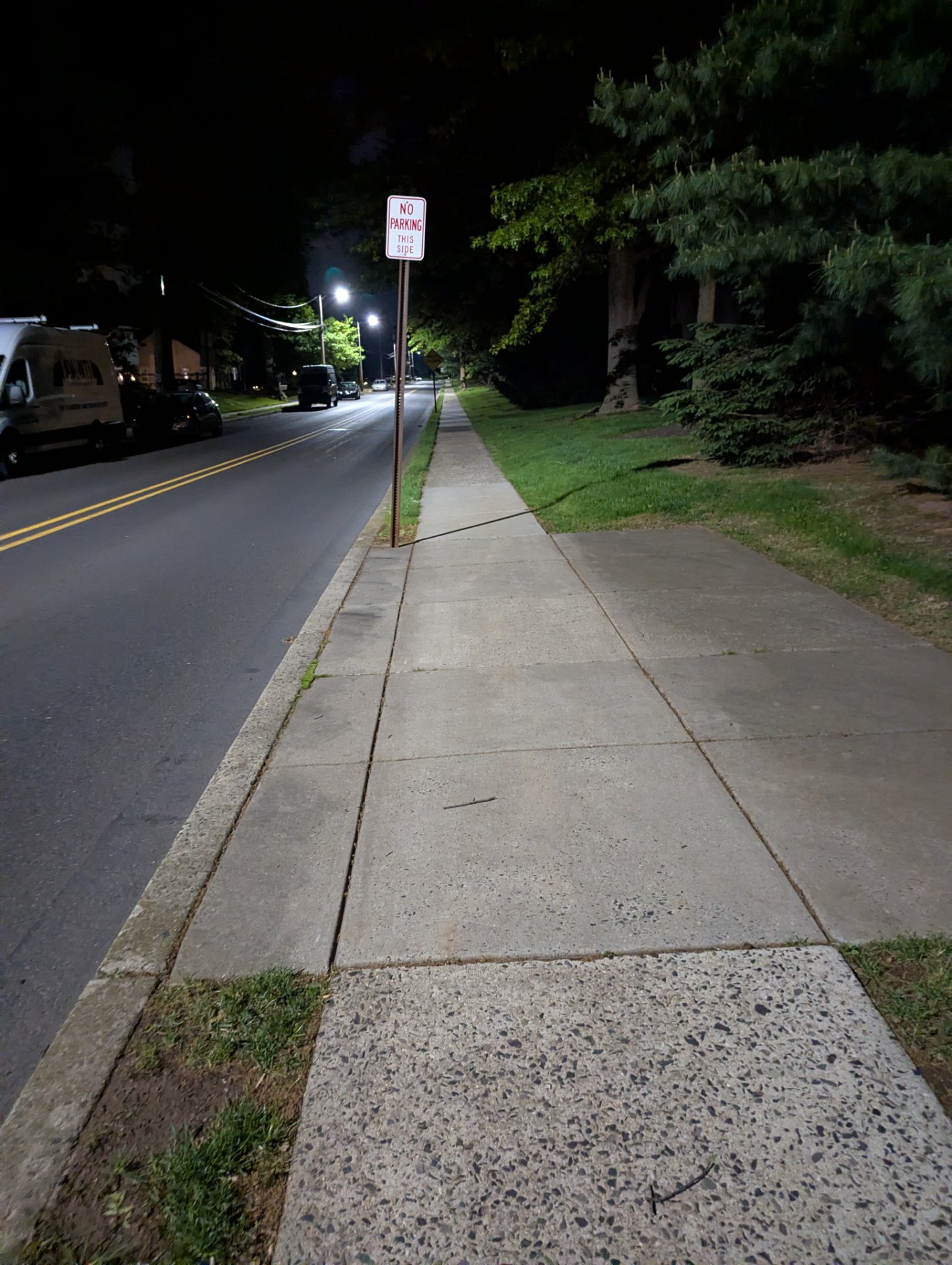 A nighttime walk or run along a residential street with a well-lit sidewalk. This appears to be an evening cardio session through a neighborhood.