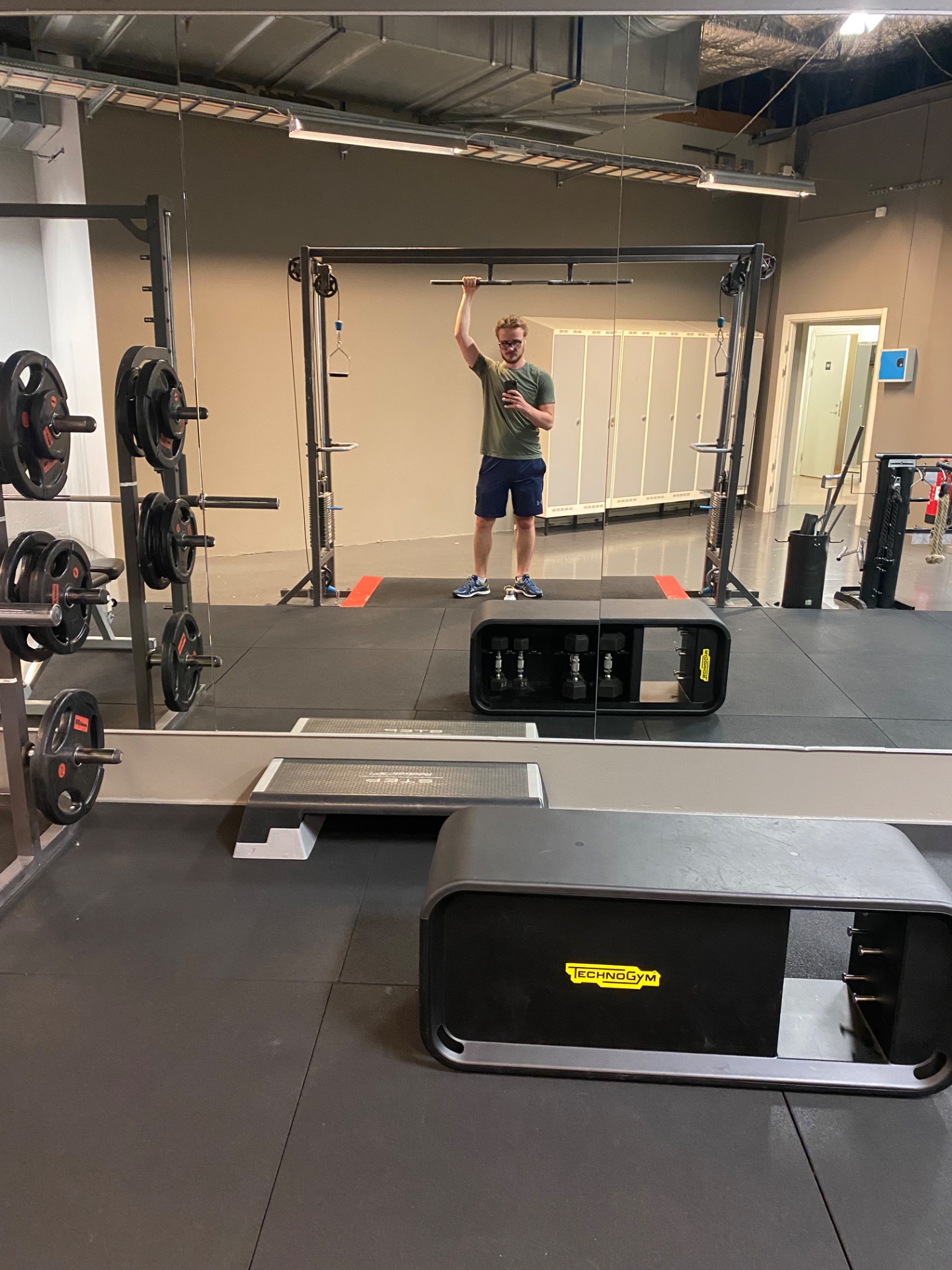 A gym workout featuring pull-up bar training and resistance exercises in a well-equipped CrossFit-style facility. The athlete is working on upper body strength with access to loaded barbells and functional training equipment.