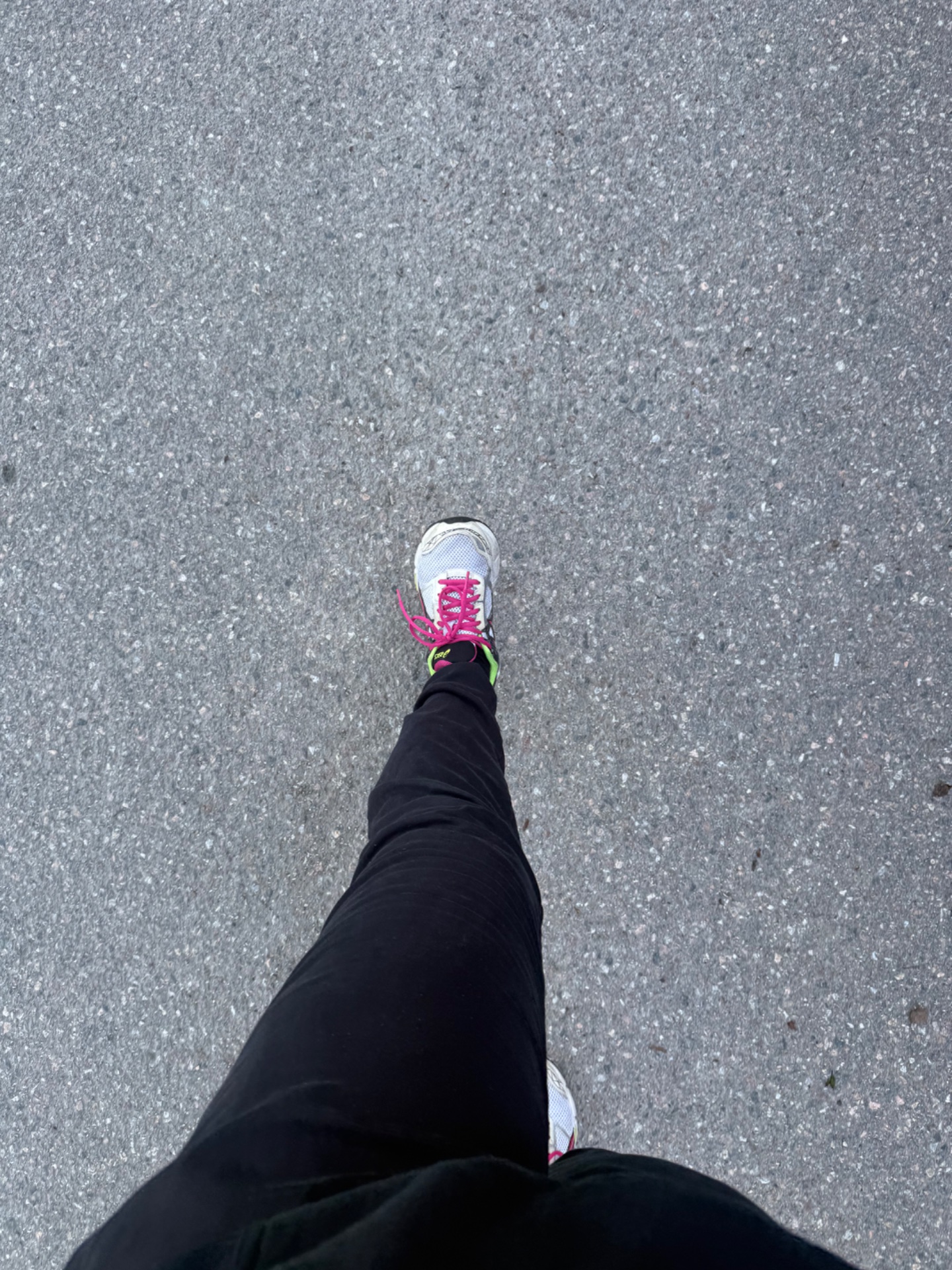 A runner's perspective shot capturing a run on asphalt pavement, featuring vibrant pink and white running shoes and black leggings. This classic running selfie shows someone actively engaged in cardio exercise outdoors!