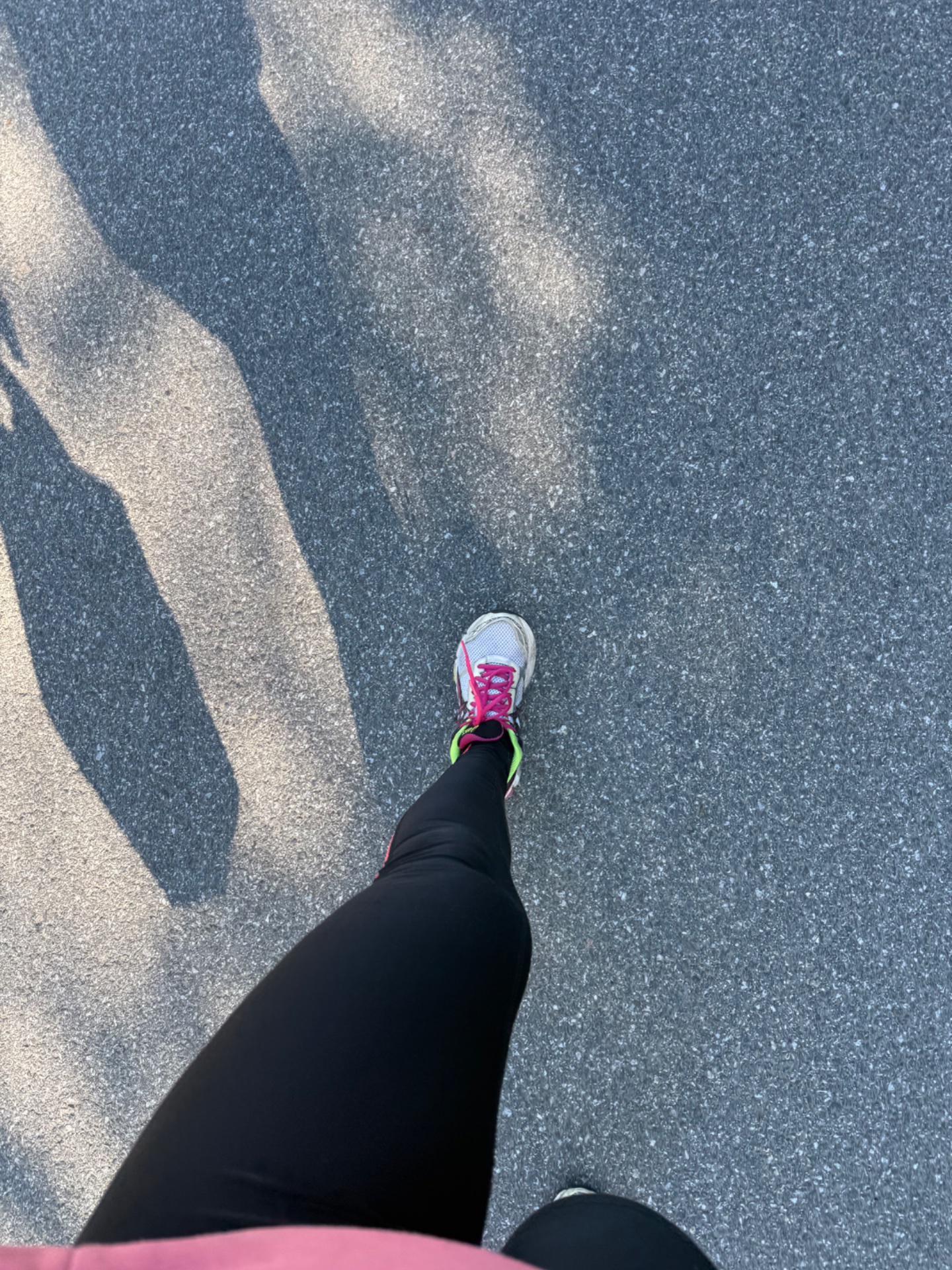 A runner capturing a first-person perspective shot during an outdoor run on a paved road, showing athletic gear and road markings below. Great form and energy!