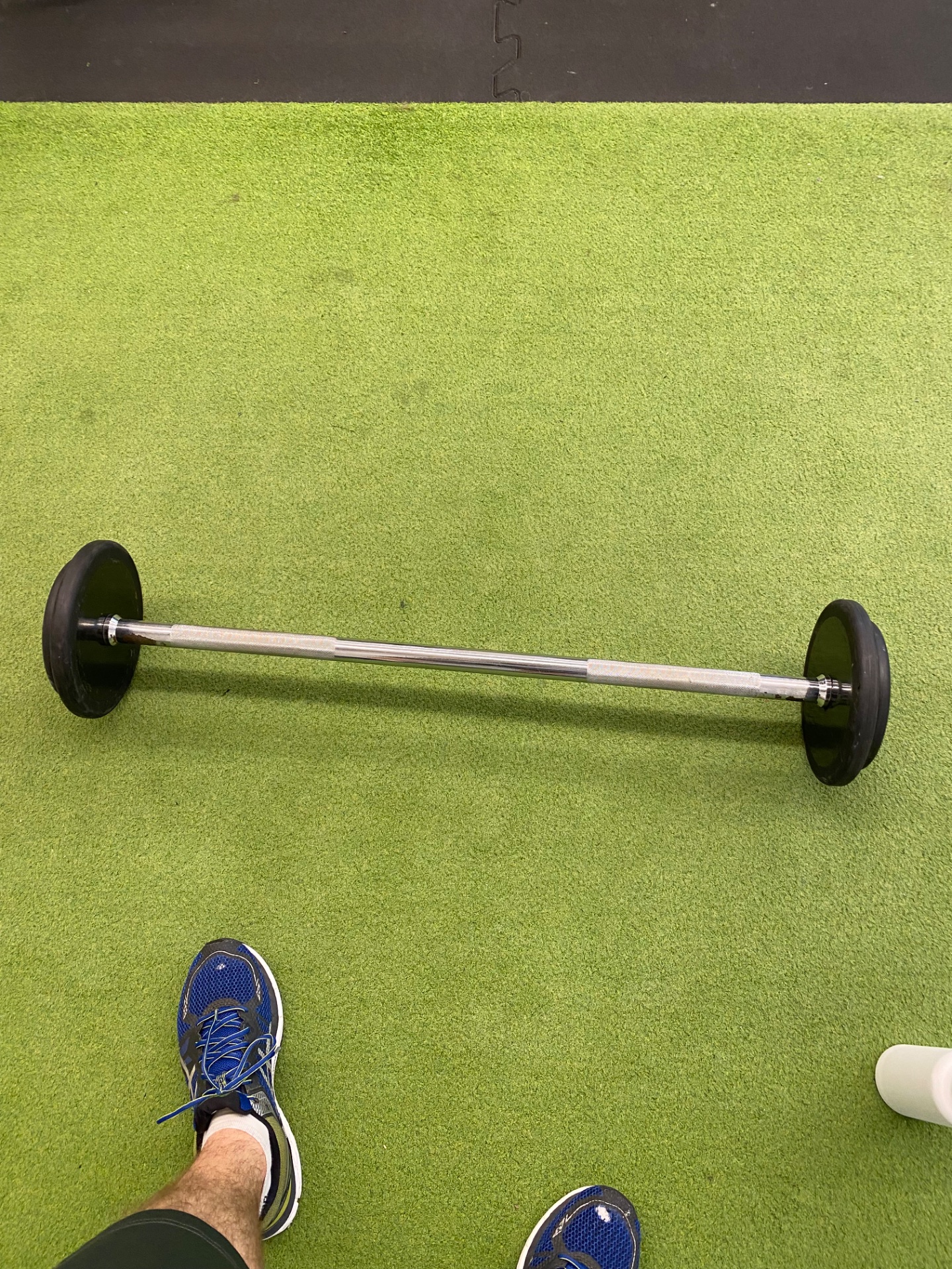 A weightlifting session with a loaded barbell ready for exercise on a gym floor. The athlete is positioned to perform a lift, showcasing resistance training work.