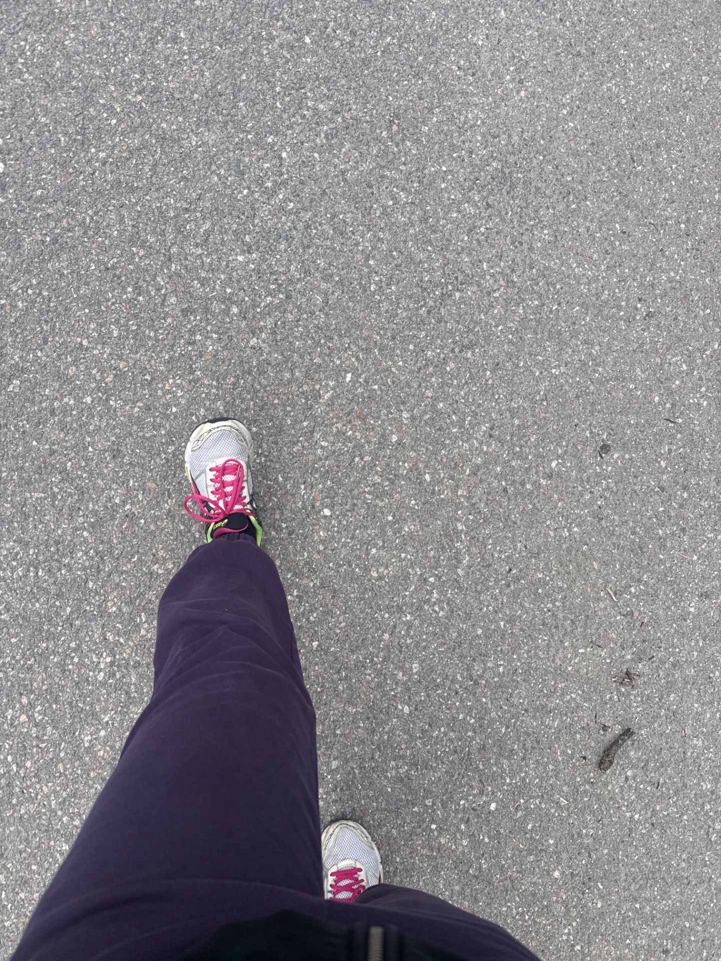 A first-person perspective of a runner in motion on pavement, wearing athletic shoes with bright pink accents and dark leggings. This classic running selfie captures an active cardio workout in progress!