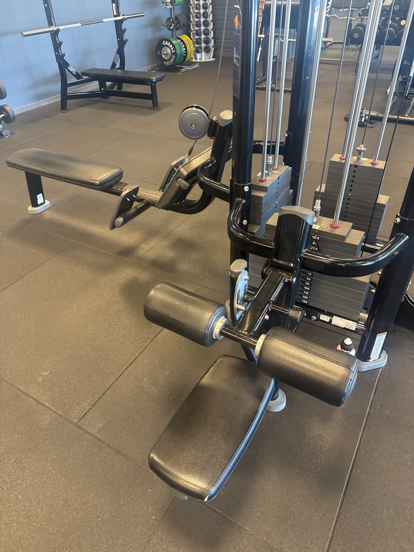 A well-equipped gym facility showcasing multiple resistance training machines, including leg press equipment with dumbbells and various cable machines. This is a dedicated strength training space ready for serious weightlifting and resistance work.