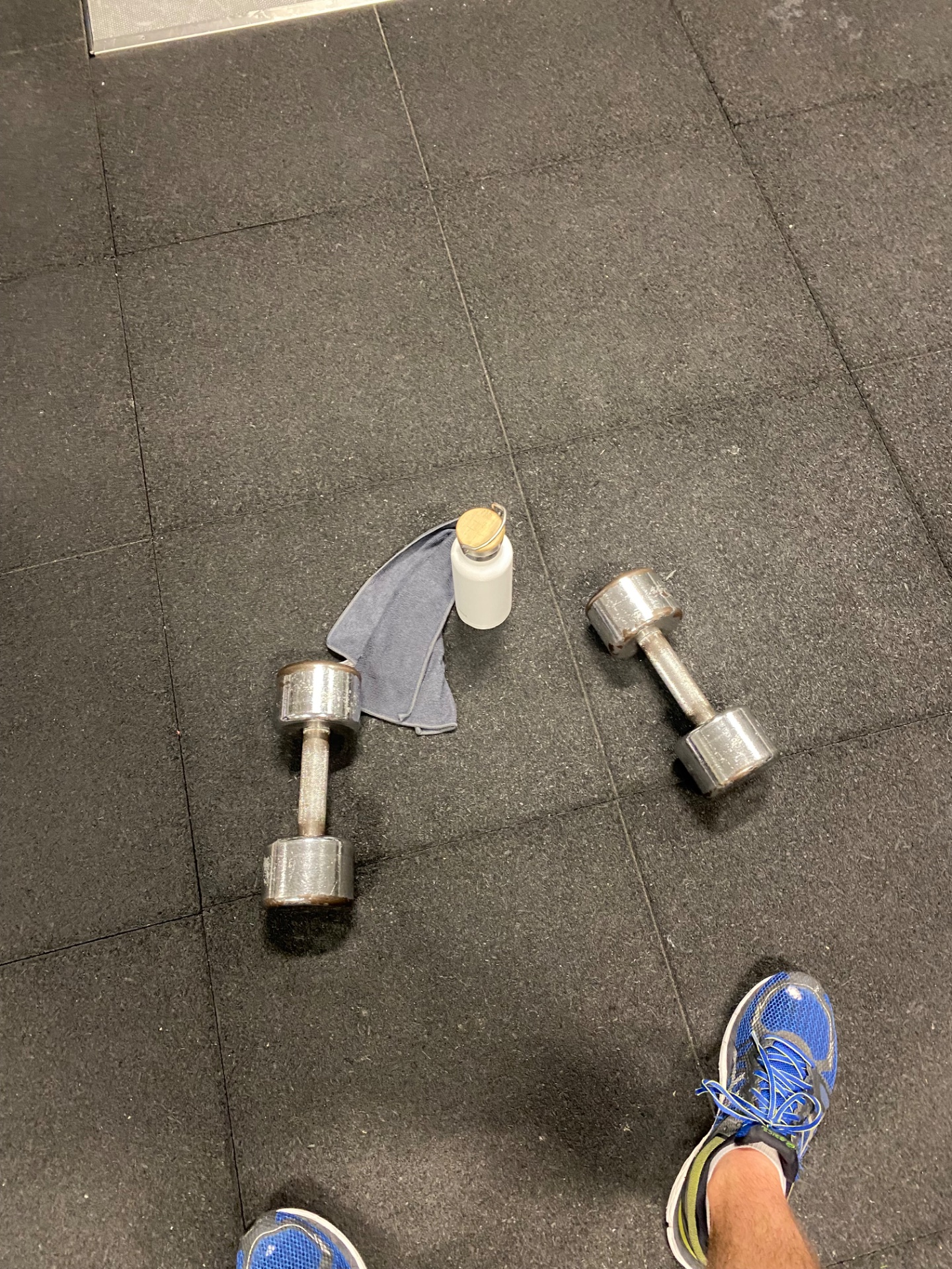 A gym workout featuring dumbbells and hydration setup on a rubber floor. This is a strength training session ready to build muscle and power!