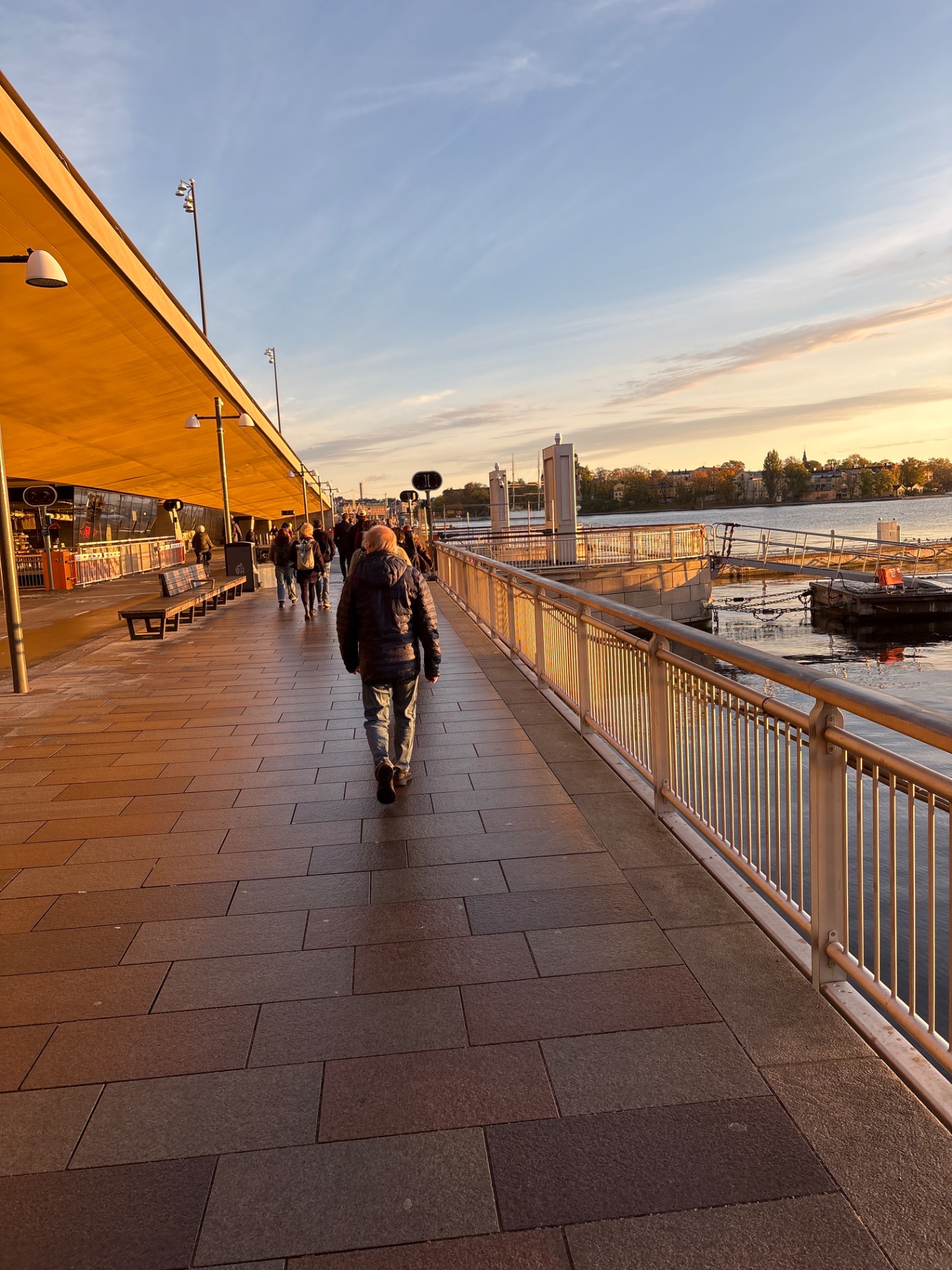 A scenic waterfront walk or jog along a beautiful promenade at sunset, with a person moving along the riverside path in what appears to be a dedicated pedestrian/exercise area.